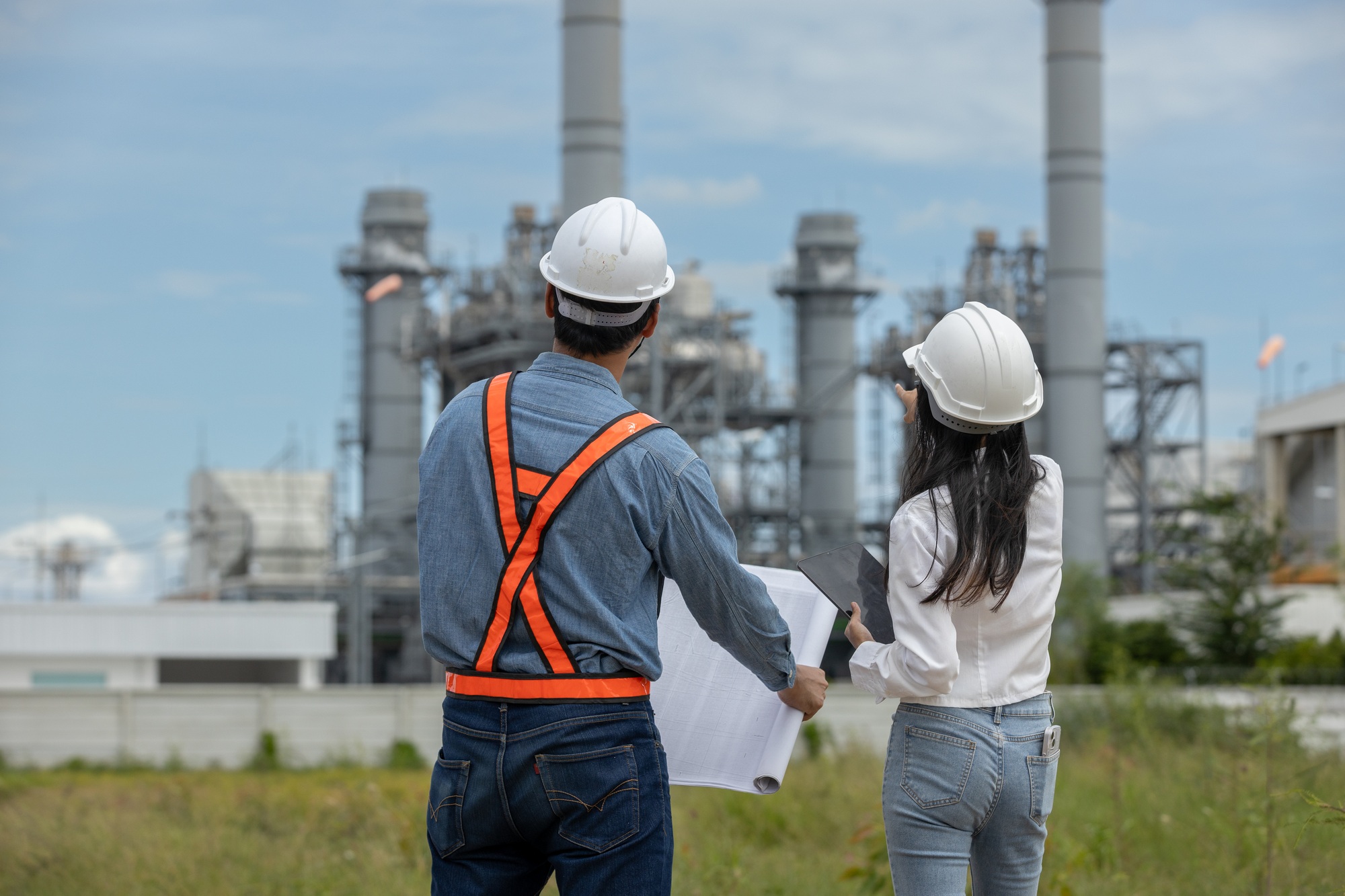 Engineer with blueprint and tablet working factory producing electricity oil energy.